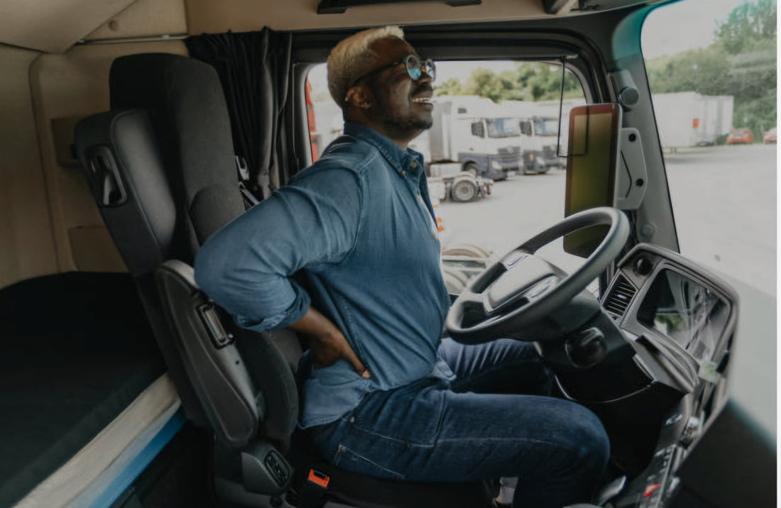 Truck driver seated in cab holding lower back in pain, representing back strain from long hours of driving and poor lumbar support.