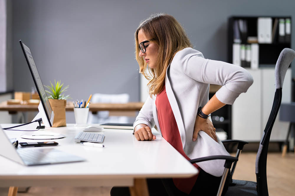 Office worker experiencing lower back pain while sitting at a desk, highlighting poor posture and lack of lumbar support.