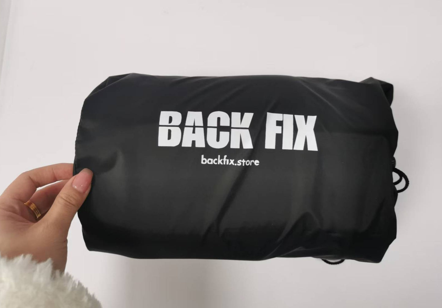 Back Fix lumbar and neck posture support inside its black storage bag with the Back Fix logo and website printed on the front. The compact packaging customers will see when unboxing.
